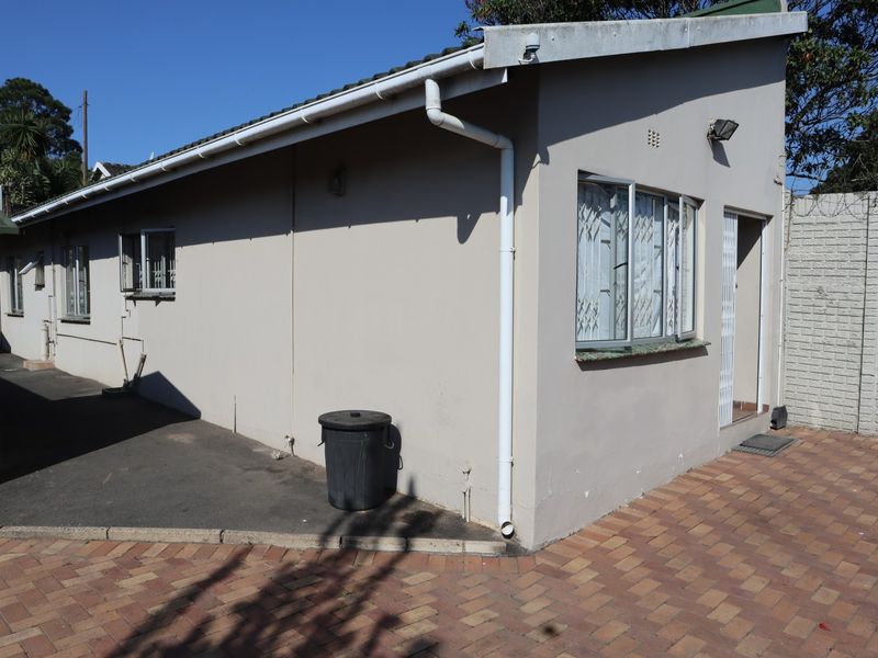 Rear exterior view of the cottage featuring paved ground, security bars on windows, and functional guttering systems.
