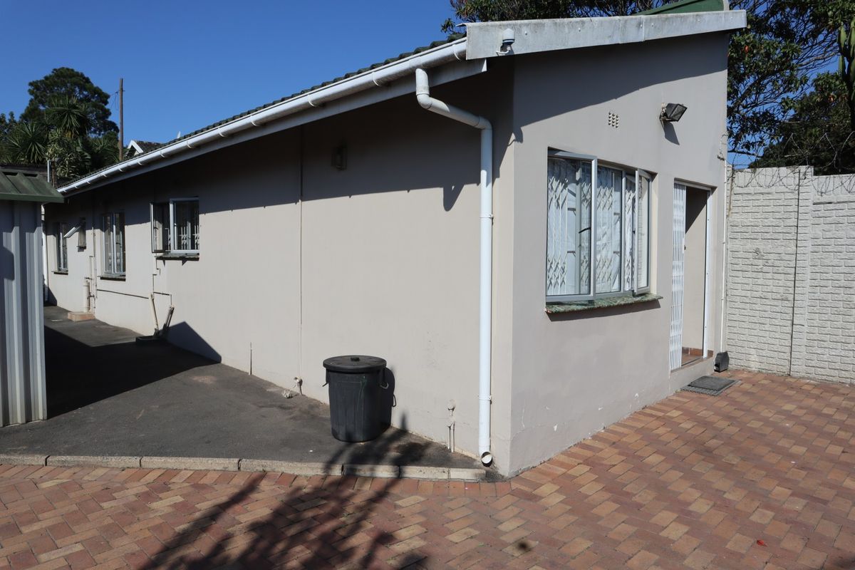 Rear exterior view of the cottage featuring paved ground, security bars on windows, and functional guttering systems.