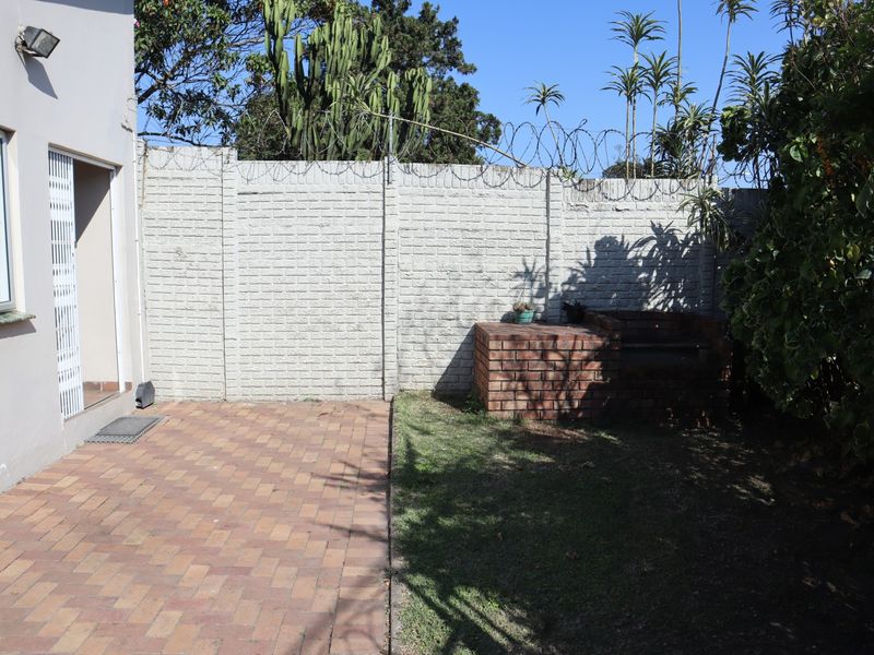 Rear garden area featuring a paved patio, a built-in brick braai, and a secure perimeter wall with razor wire.