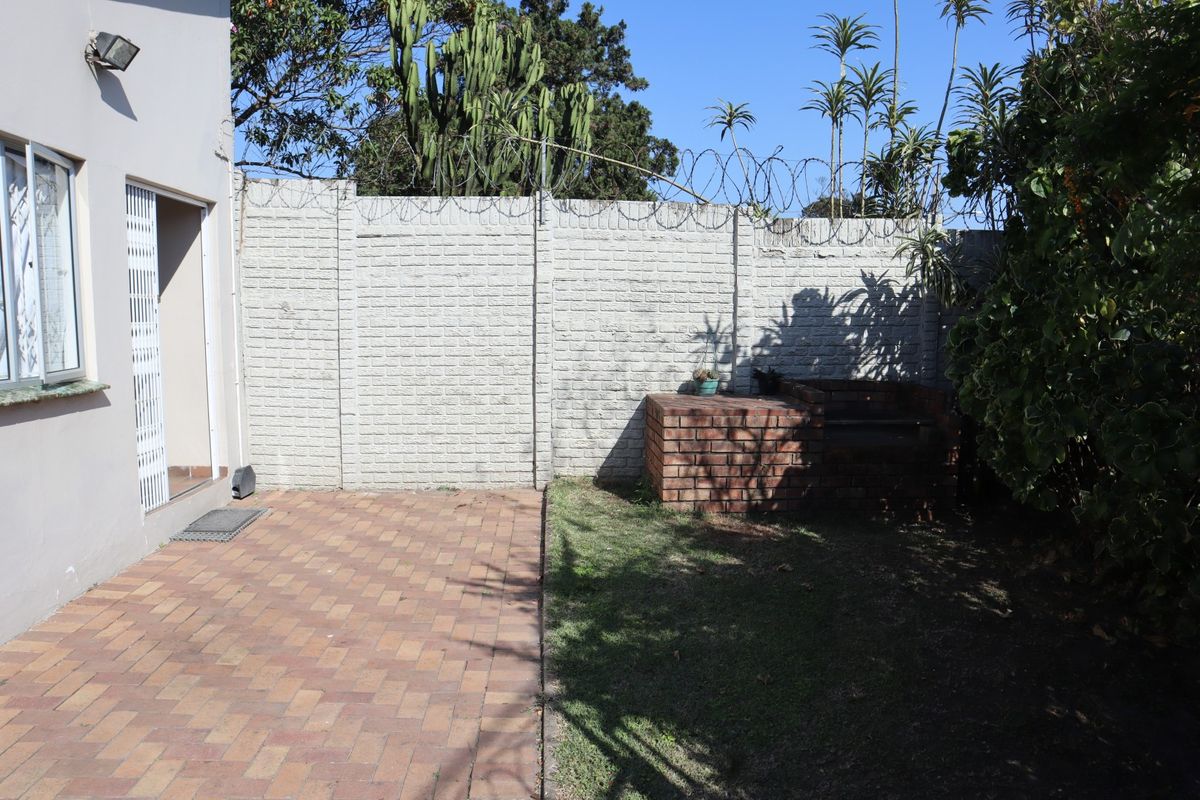 Rear garden area featuring a paved patio, a built-in brick braai, and a secure perimeter wall with razor wire.