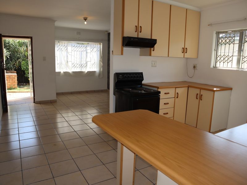 Open-plan kitchen and living area featuring tiled floors, dated cabinetry, and direct access to the rear garden through a security-fitted door.