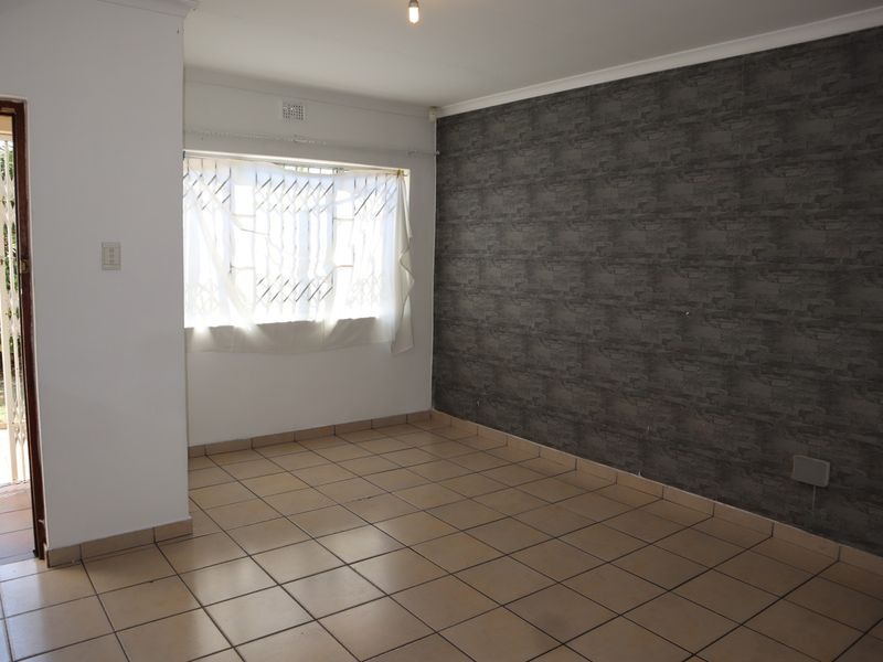 An empty living room featuring tiled flooring, a dark textured feature wall, and direct access to the exterior through a security gate.