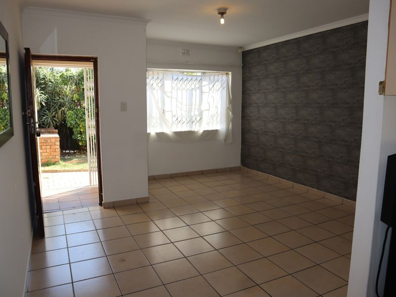 An empty living room featuring ceramic floor tiles, a dark feature wall, and direct access to an outdoor patio area through a security gate.