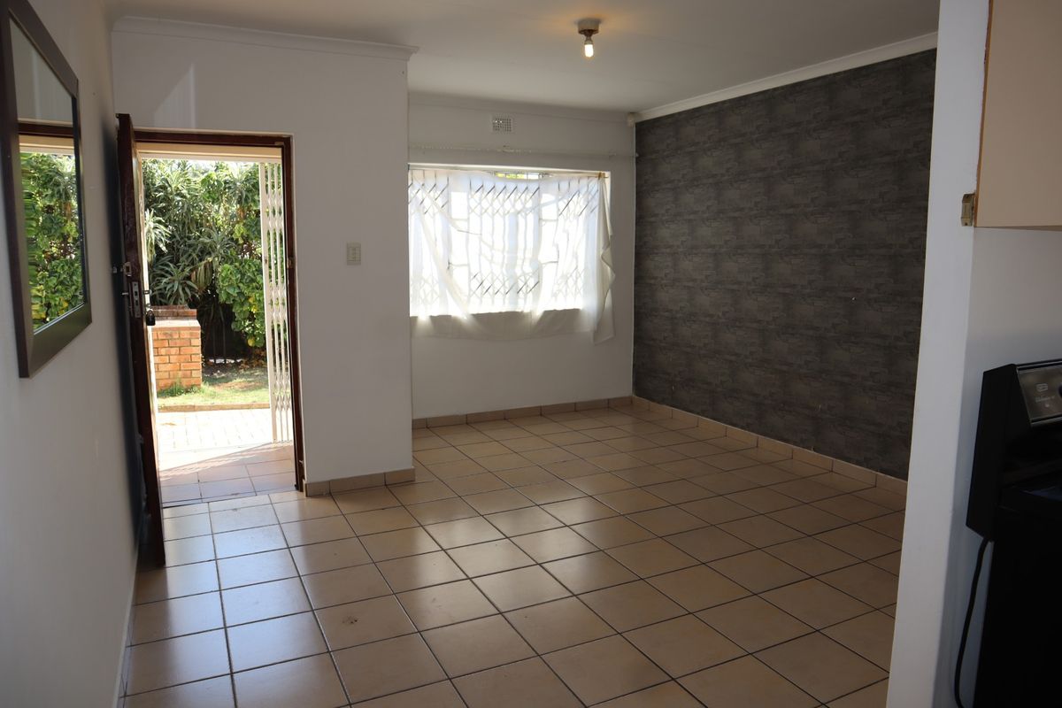 An empty living room featuring ceramic floor tiles, a dark feature wall, and direct access to an outdoor patio area through a security gate.