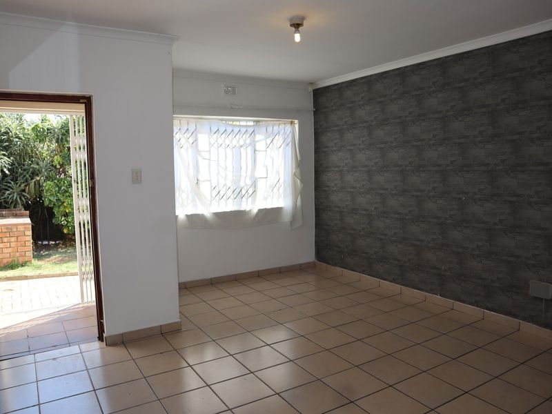 An empty living room featuring tiled flooring, a dark textured accent wall, and direct access to the exterior through a security gate.