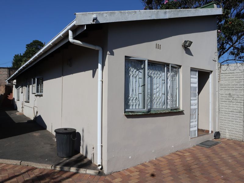 Rear exterior view of the cottage featuring paved ground, security gates, and standard window fixtures with security bars.