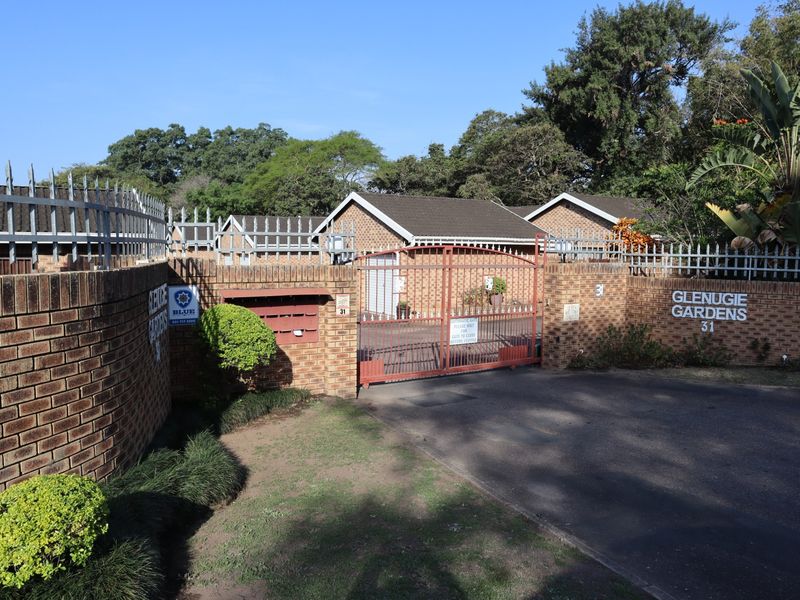 Front entrance view of Glenugie Gardens townhouse complex featuring a brick boundary wall, security fencing, and an automated access gate.