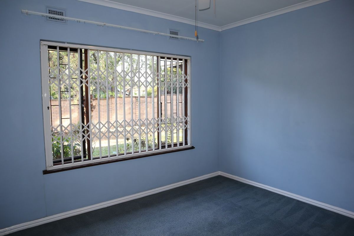 An empty bedroom featuring blue walls, carpeted flooring, and a window fitted with a white security gate.