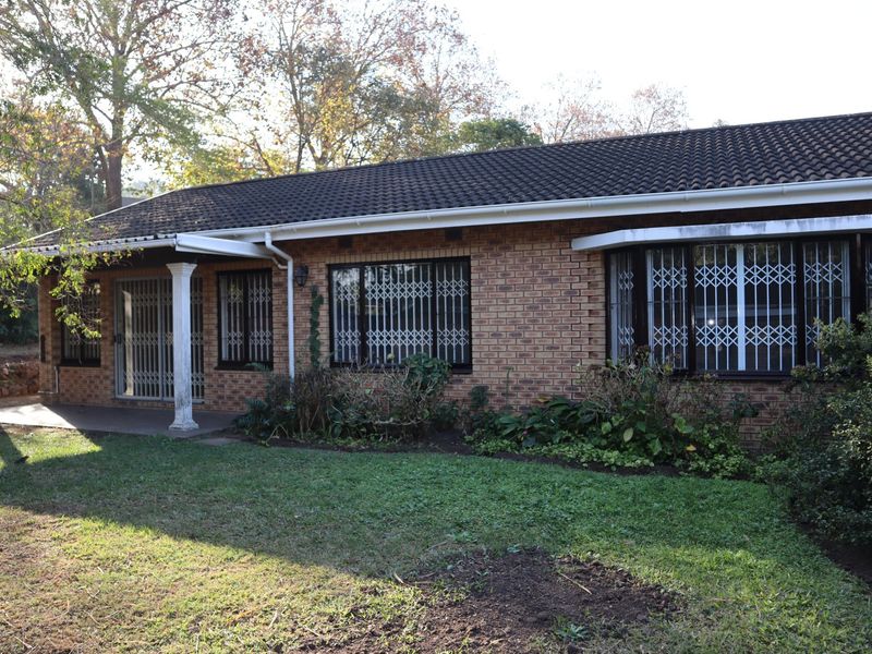 Rear view of a brick townhouse featuring a covered patio, security gates on windows, and a private garden area.