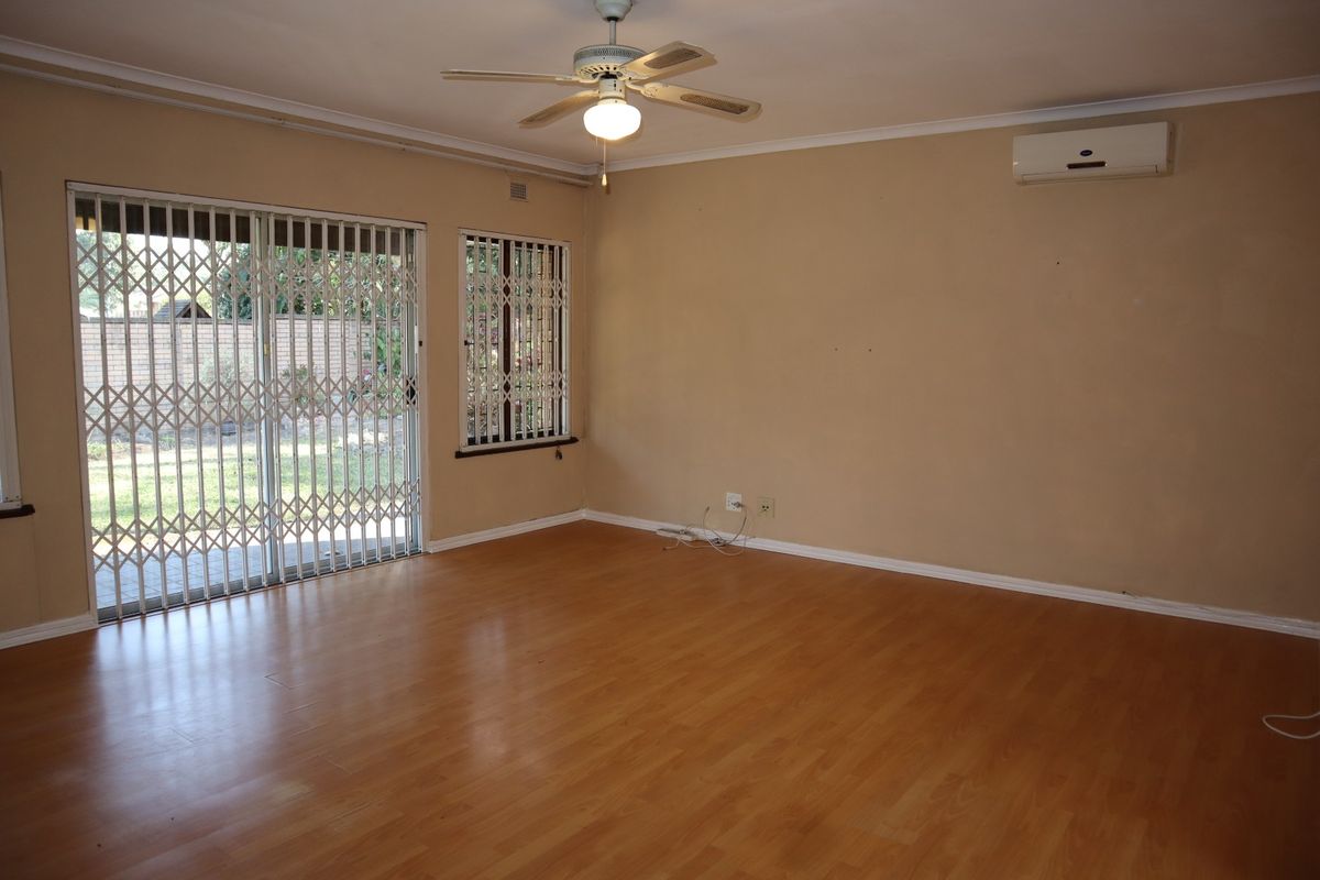 Spacious living area featuring laminate flooring, a ceiling fan, and a wall-mounted air conditioning unit, with direct access to the garden through sliding doors.