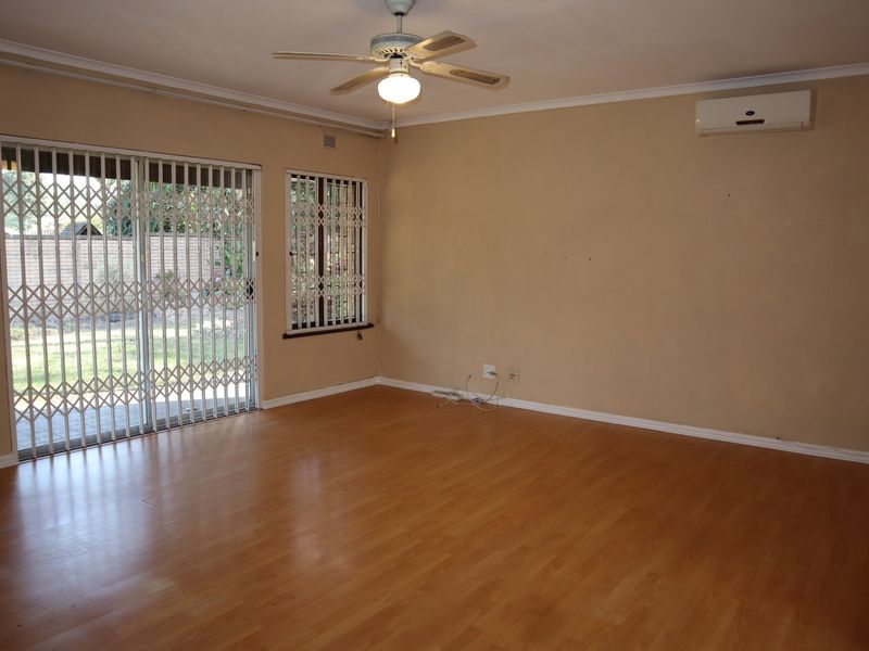 Spacious living area featuring laminate flooring, a ceiling fan, and a wall-mounted air conditioning unit, with direct access to the garden through sliding doors.