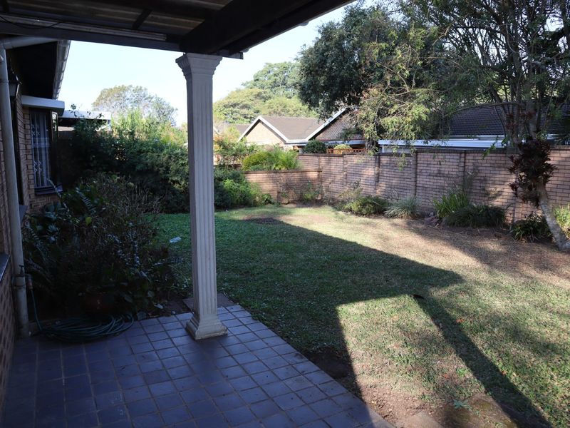 A covered patio area overlooking a private garden with a brick boundary wall and decorative column support.
