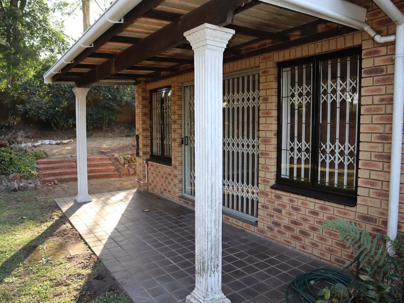 Covered brick patio area featuring decorative columns, timber pergola, and secure access points, overlooking a garden space.