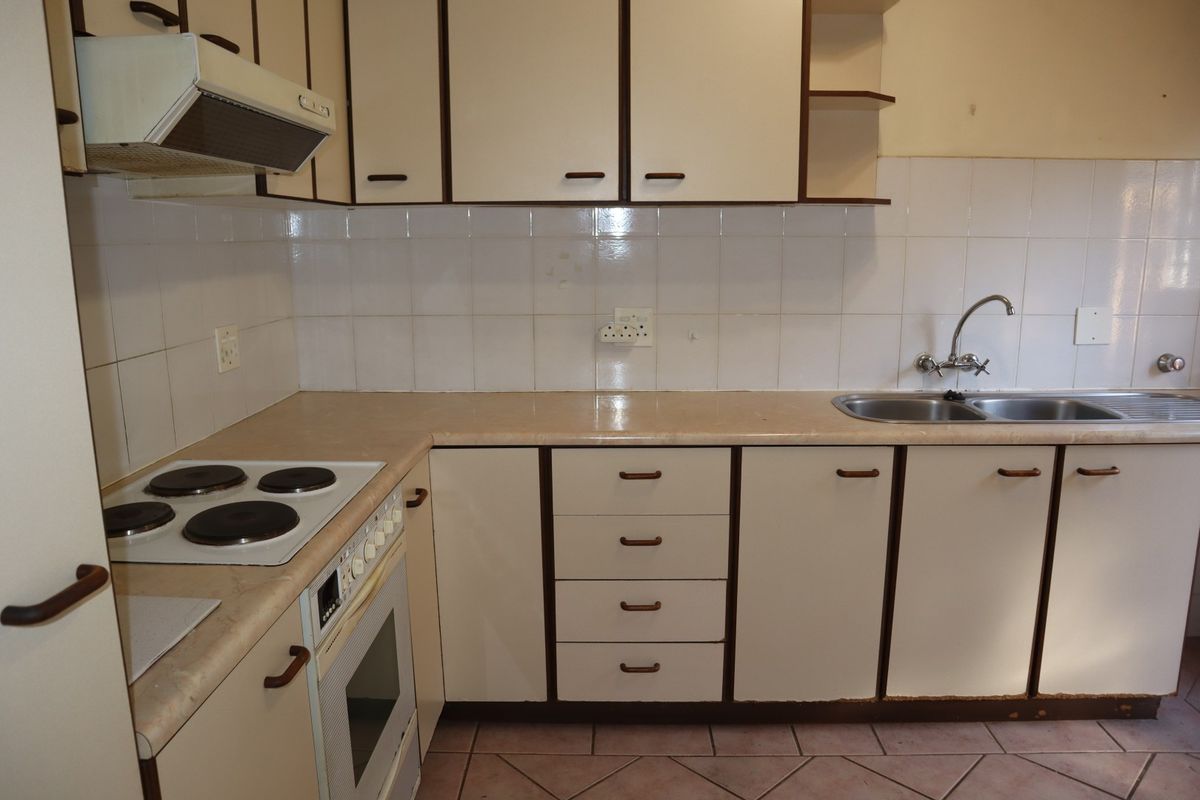 A functional kitchen featuring built-in cabinetry, laminate countertops, a stainless steel sink, and integrated electric cooking appliances with a tiled backsplash.