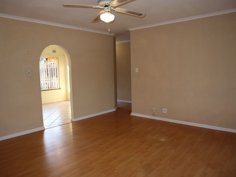 An empty living room featuring laminate flooring, a ceiling fan, and a classic arched doorway leading to an adjacent space.