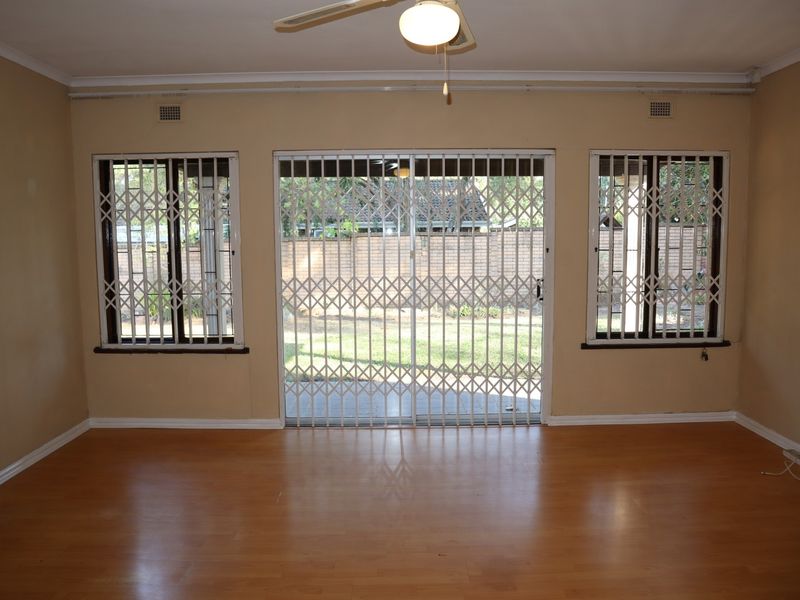 Spacious living room featuring laminate flooring, a ceiling fan, and security gates leading to the rear garden area.