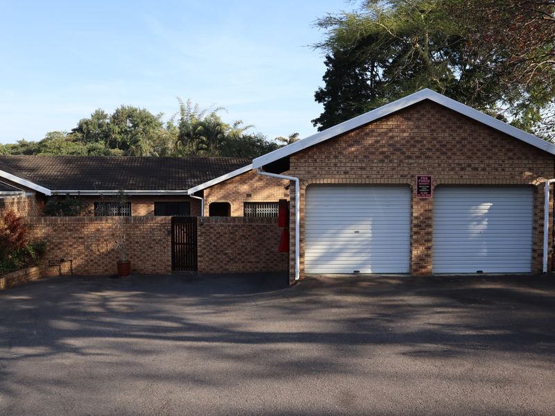 Front view of a townhouse featuring a double garage with white roller doors, brick exterior, and a paved driveway.