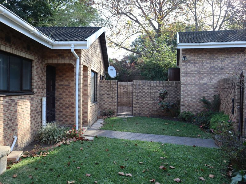 A private rear courtyard featuring a paved walkway, established lawn, and face brick exterior walls, providing a secure and low-maintenance outdoor space.