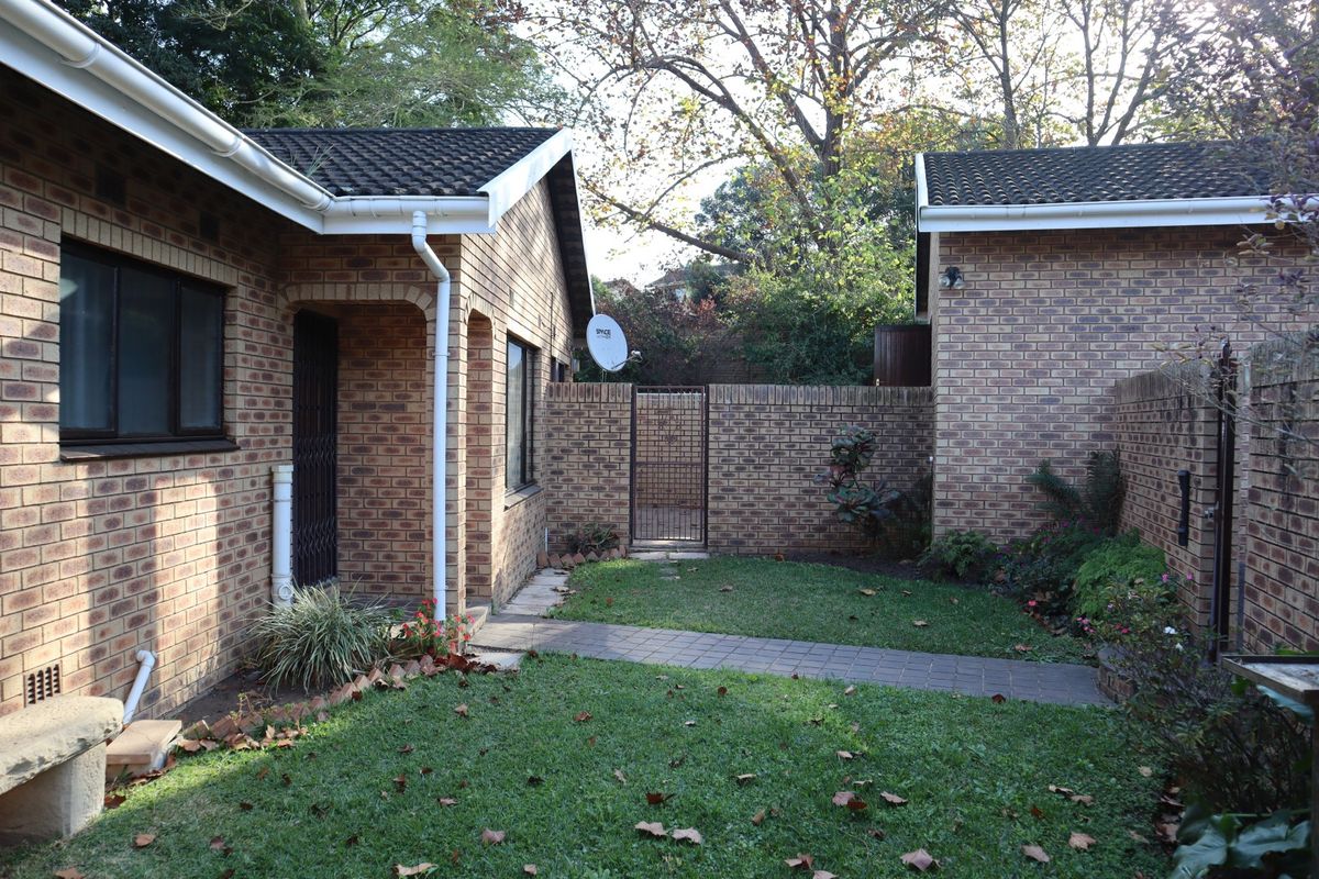 A private rear courtyard featuring a paved walkway, established lawn, and face brick exterior walls, providing a secure and low-maintenance outdoor space.