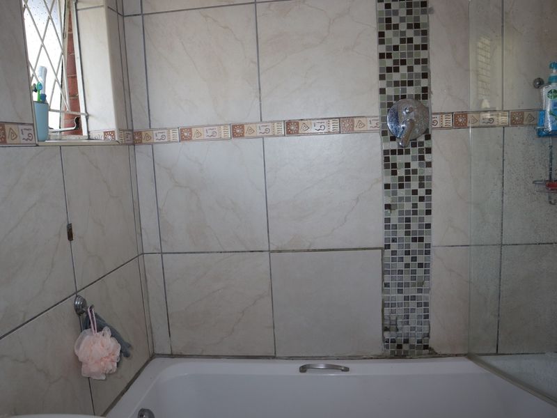 A bathroom featuring a bathtub with a shower mixer, accented by a decorative mosaic tile feature wall and neutral ceramic wall tiles.