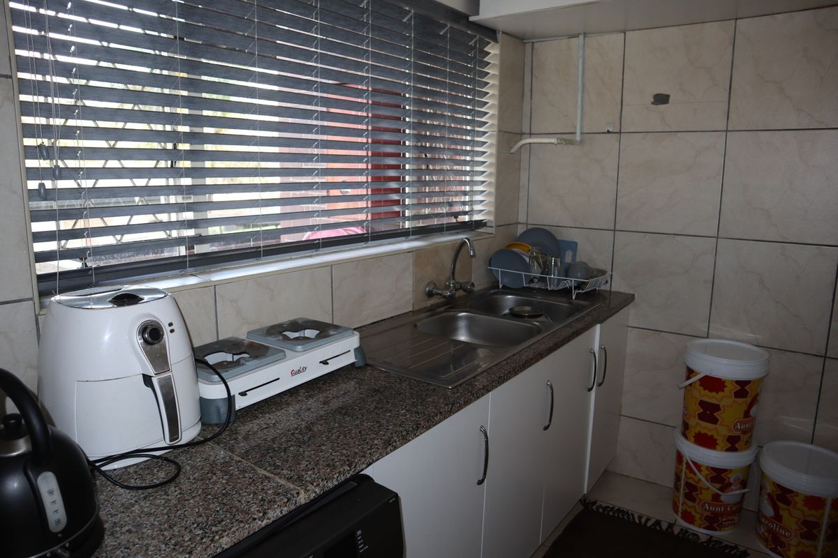 A functional kitchen area featuring granite countertops, a stainless steel double sink, tiled splashbacks, and built-in cabinetry with venetian blinds.
