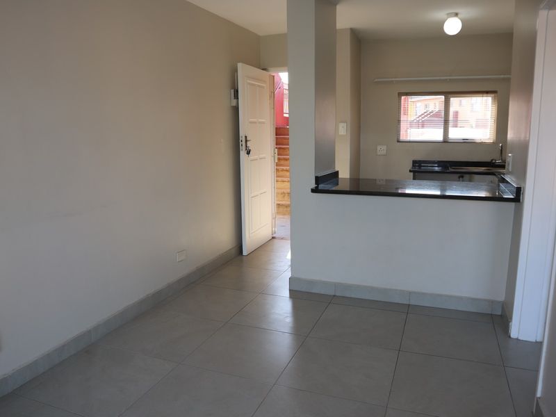 An open-plan living and kitchen area featuring neutral tiled flooring, granite countertops, and direct access to an exterior entrance.