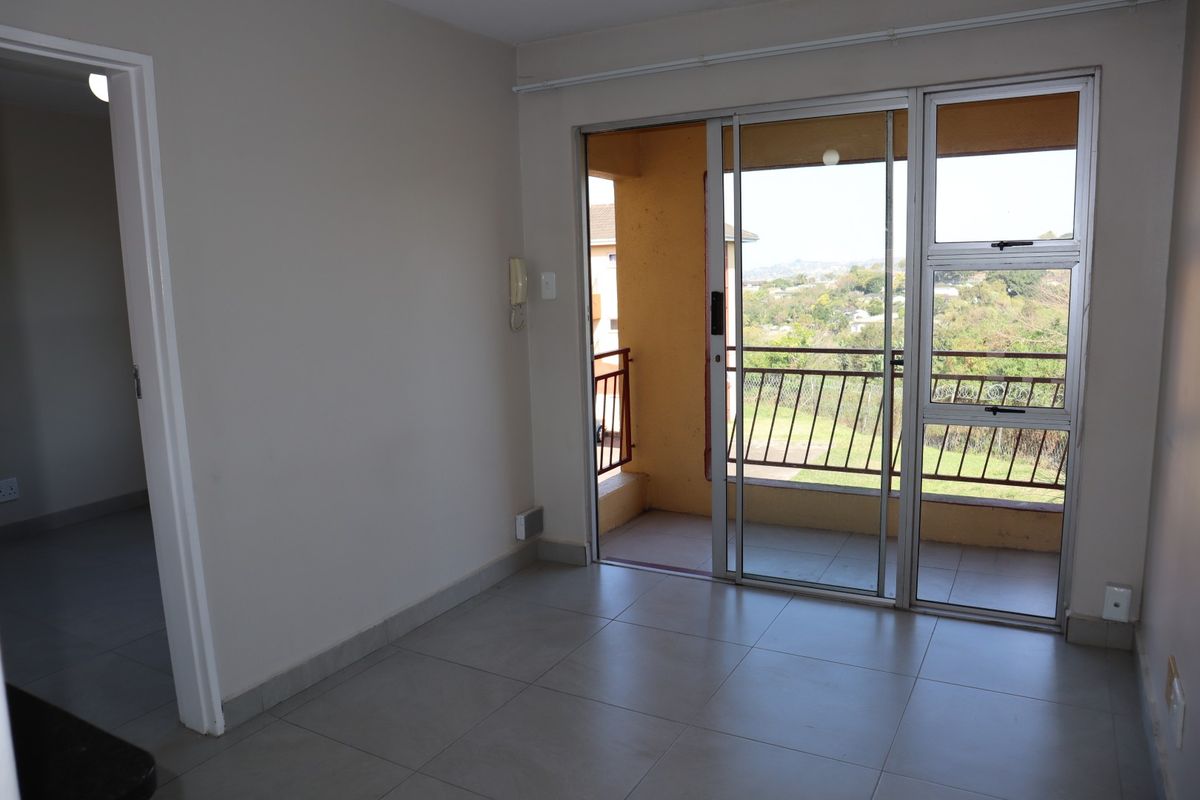 An empty living room featuring tiled flooring and a sliding glass door that provides access to a balcony with scenic views.