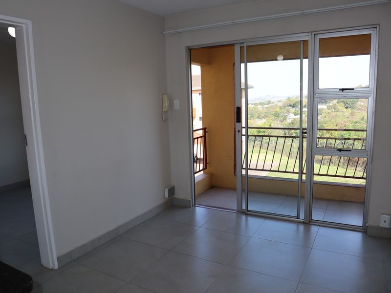 An empty living room featuring tiled flooring and a sliding glass door that provides access to a balcony with scenic views.