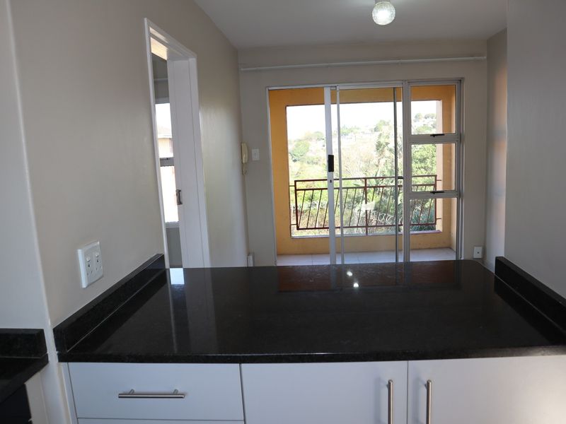 Open plan kitchen area featuring dark granite countertops and white cabinetry, leading directly to a balcony with scenic views.