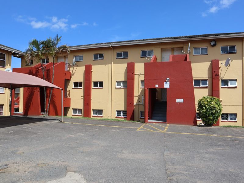 Exterior view of a multi-story apartment complex featuring a paved parking area with a shade port and external staircases.