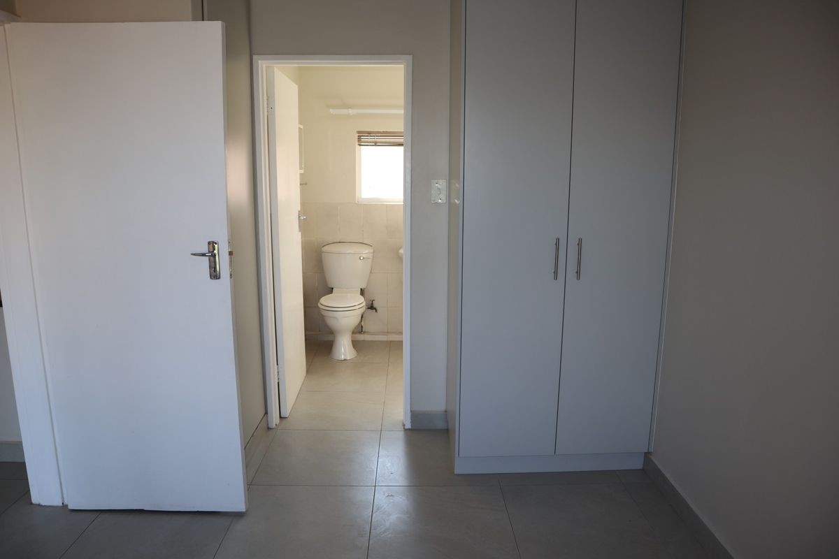 A clean, neutral bedroom featuring tiled flooring, a built-in wardrobe, and direct access to an en-suite bathroom.