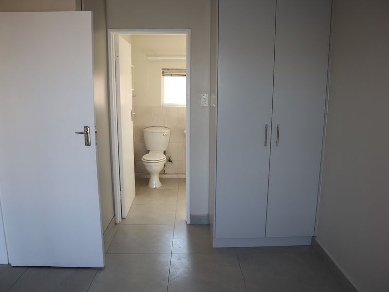 A clean, neutral bedroom featuring tiled flooring, a built-in wardrobe, and direct access to an en-suite bathroom.