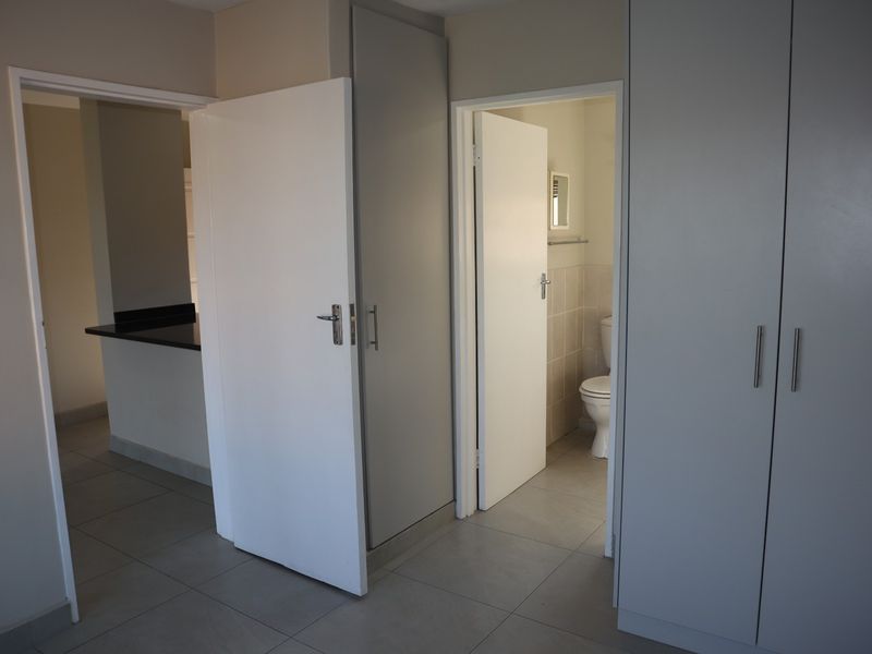 A clean, neutral hallway featuring built-in cupboards, tiled flooring, and access to an adjacent kitchen and bathroom.