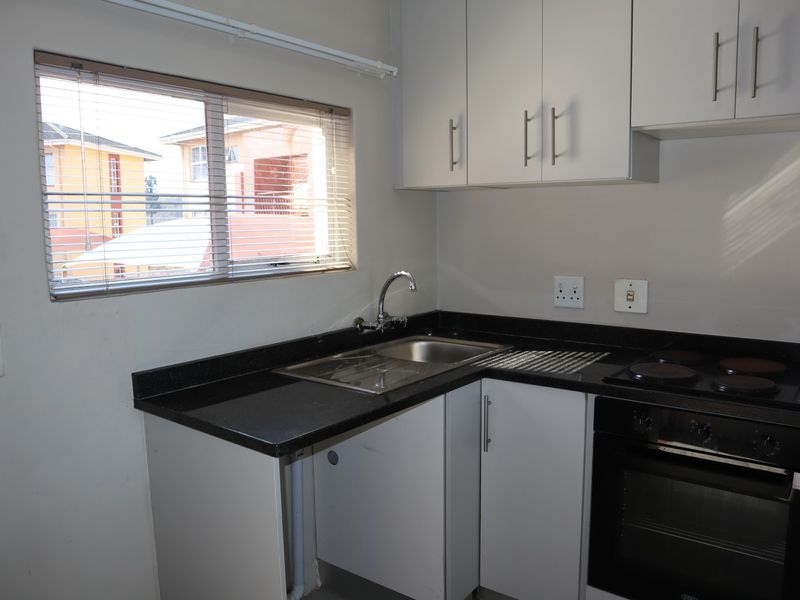 A compact, functional kitchen featuring built-in cabinetry, granite countertops, a stainless steel sink, and integrated electric oven and hob.