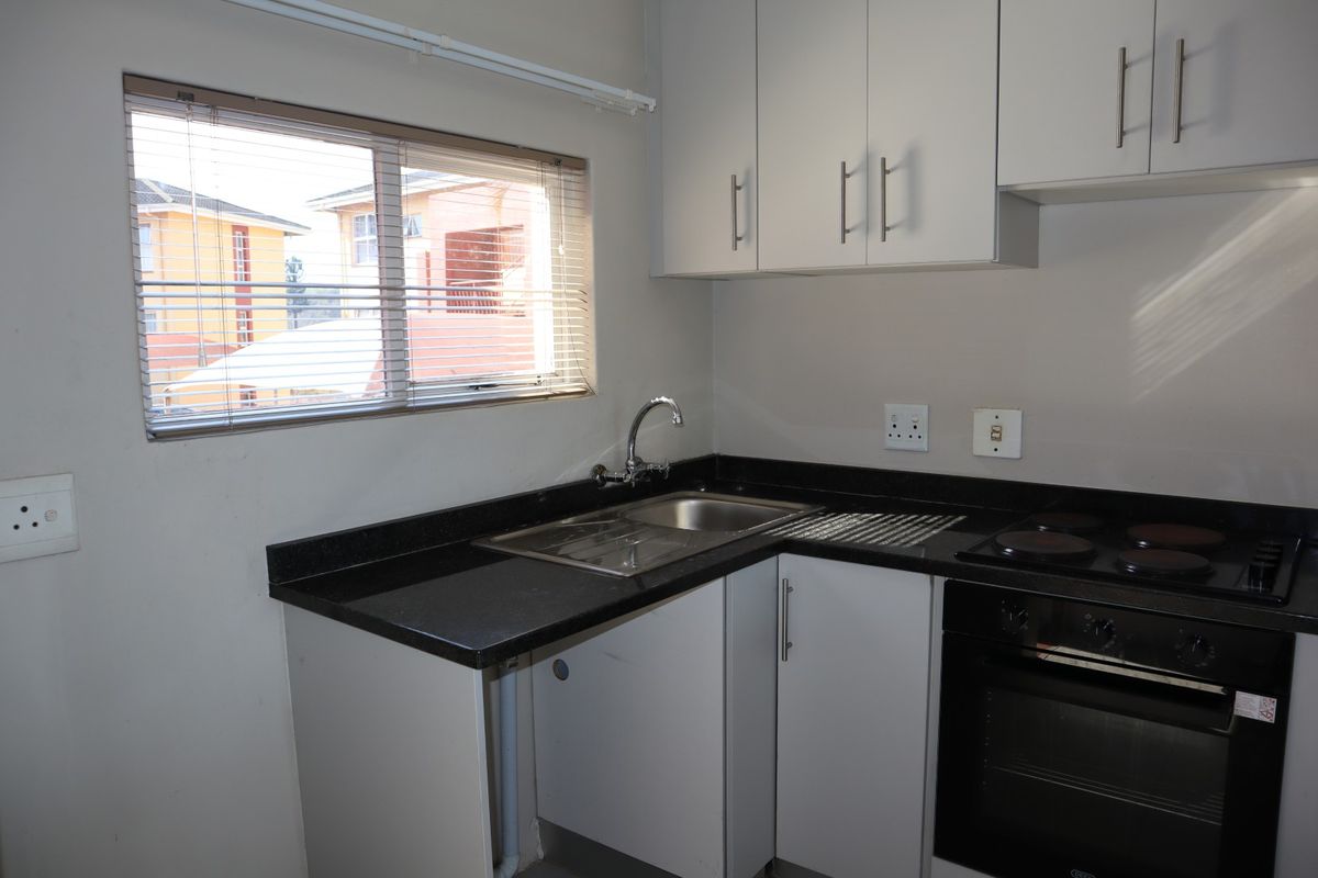 A compact, functional kitchen featuring built-in cabinetry, granite countertops, a stainless steel sink, and integrated electric oven and hob.