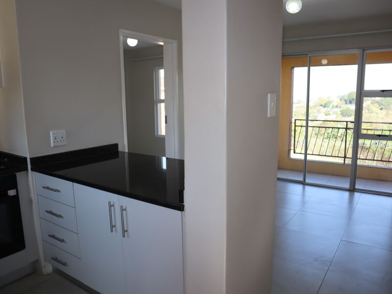 Open plan kitchen with granite countertops and built-in oven, flowing into a living area with sliding doors leading to a balcony.