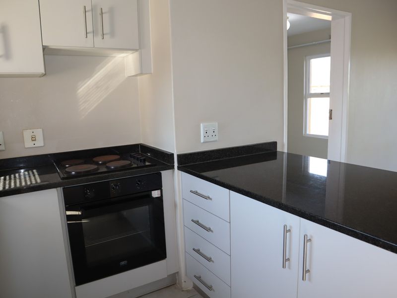 A clean, modern kitchen featuring white cabinetry, contrasting black granite countertops, and a built-in electric oven and hob.