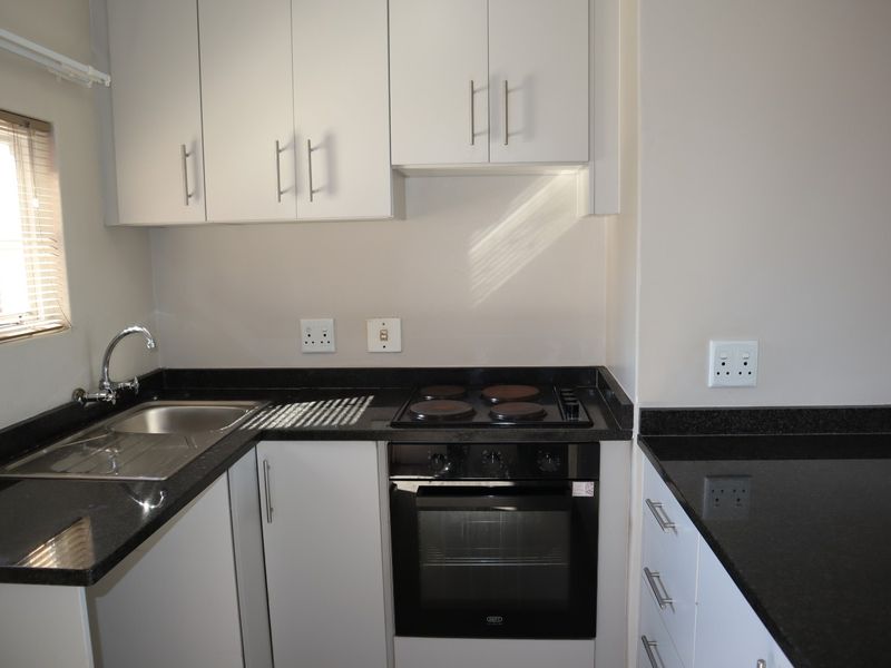 A clean, modern kitchen featuring white cabinetry, black granite countertops, a built-in oven, electric hob, and a stainless steel sink.
