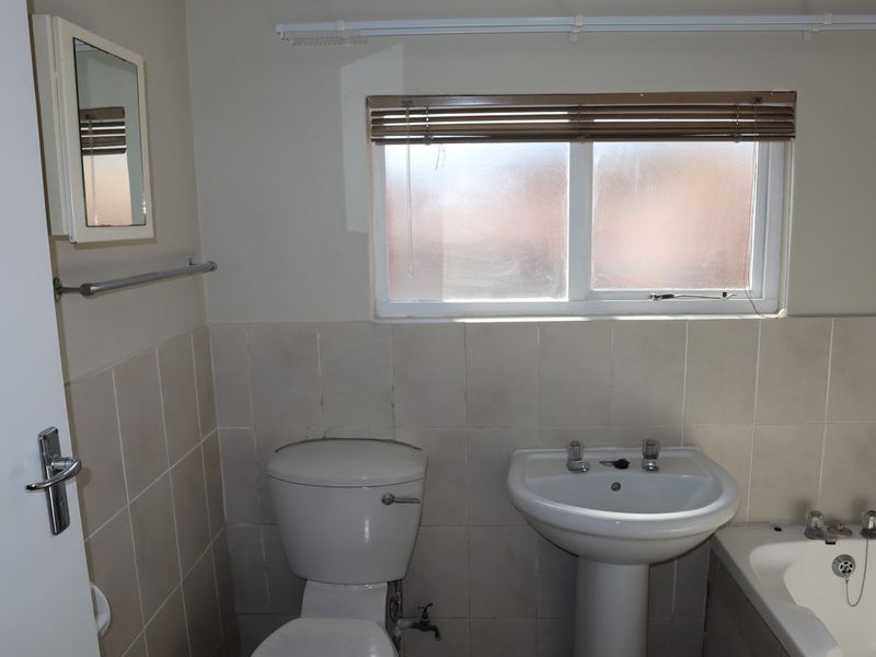 A functional bathroom featuring a pedestal basin, toilet, and bathtub with neutral wall tiling and a window for natural light.