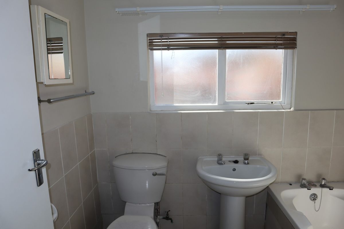 A functional bathroom featuring a pedestal basin, toilet, and bathtub with neutral wall tiling and a window for natural light.