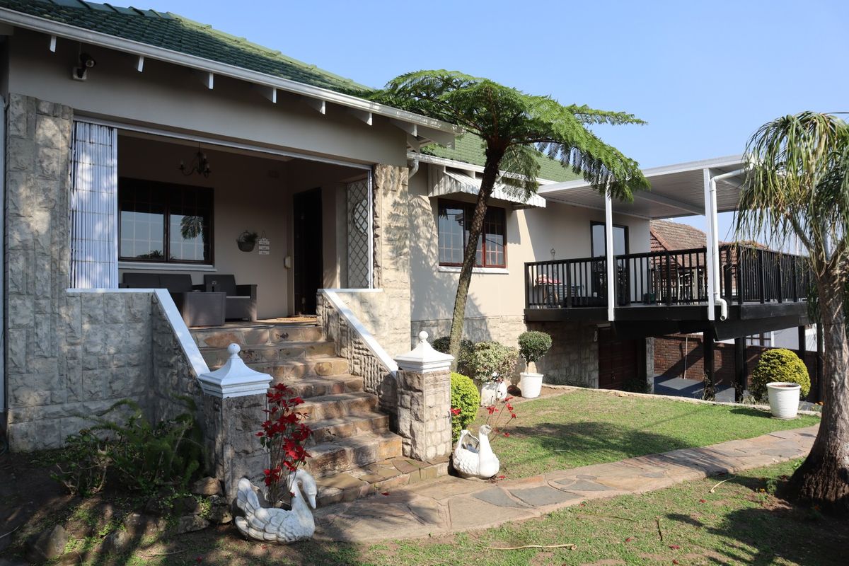 Rear view of the house featuring a stone-clad facade, raised patio entrance with stone stairs, and an elevated deck area overlooking the garden.