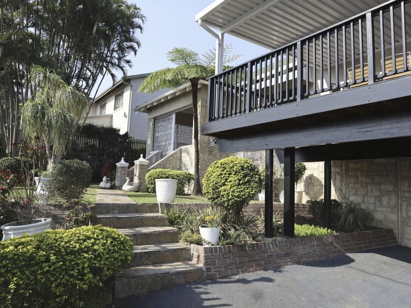 Front exterior view featuring a raised timber deck, stone-clad facade, brick retaining walls, and a landscaped garden path leading to the entrance.