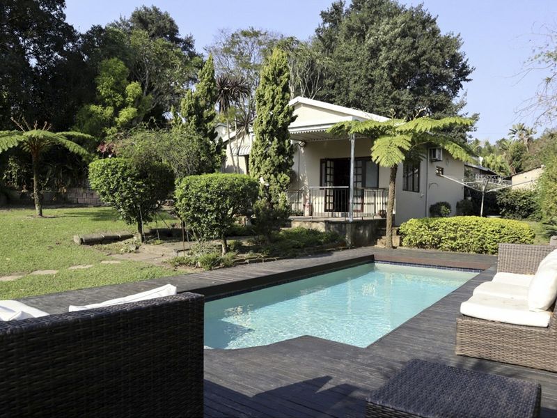A well-maintained outdoor area featuring a swimming pool with timber decking, a covered patio, and a lush, landscaped garden.
