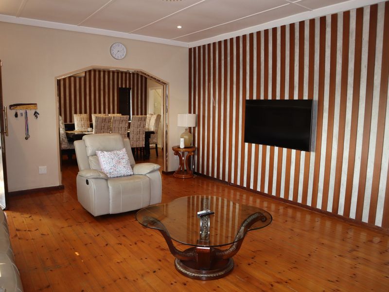 Spacious living room featuring polished timber flooring, a decorative striped feature wall, and an open archway leading to the adjacent dining area.
