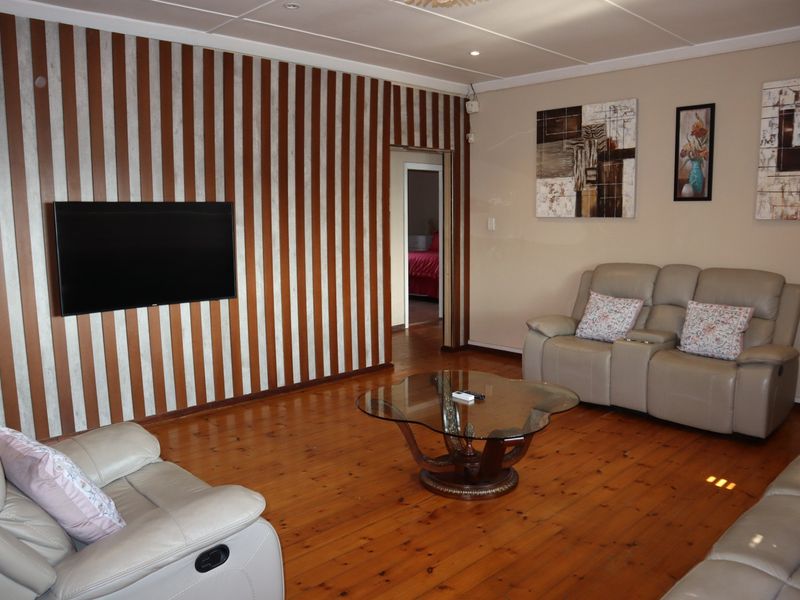 A living room featuring polished timber flooring, recessed downlighting, and a distinctive striped feature wall.