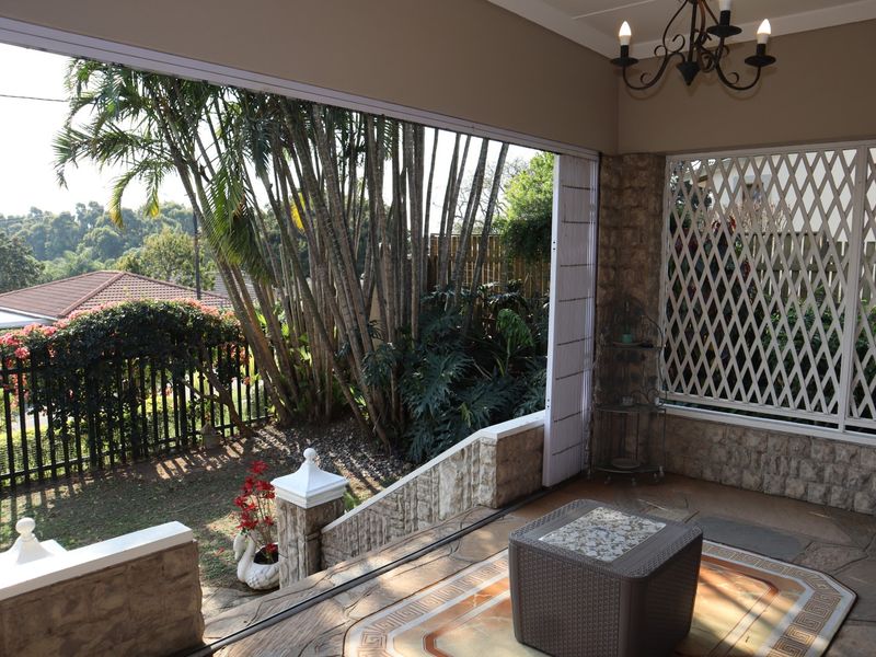A covered patio area featuring stone cladding, a decorative chandelier, and a security gate, offering a pleasant view of the garden.