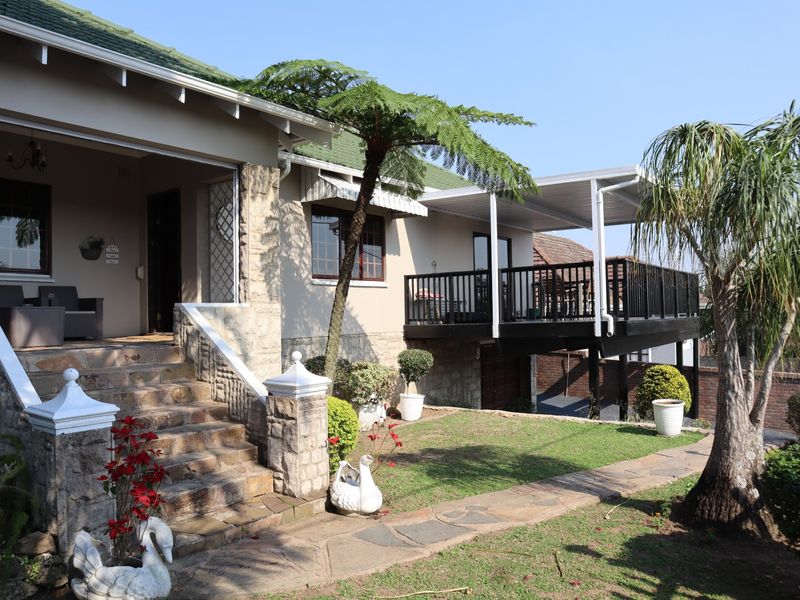 Rear view of the property featuring a stone staircase leading to a covered patio and an elevated timber deck overlooking the garden.
