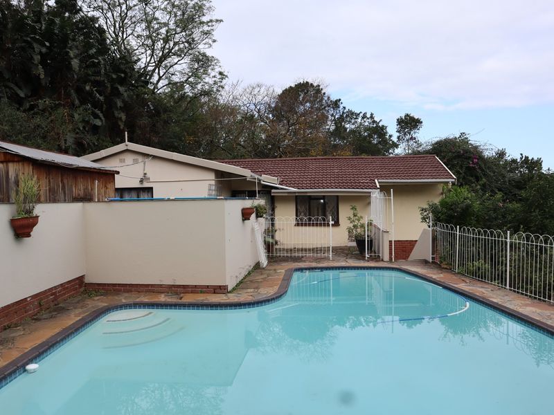 Rear exterior view featuring a swimming pool with paved surround, metal fencing, and a single-story dwelling with a tiled roof.