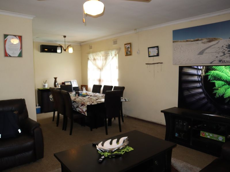 Open plan living and dining area featuring carpeted flooring, ceiling fan, and wall-mounted air conditioning unit.