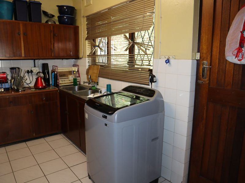 A functional laundry area featuring built-in wooden cabinetry, a stainless steel sink, tiled splashbacks, and tiled flooring with direct access to an exterior door.